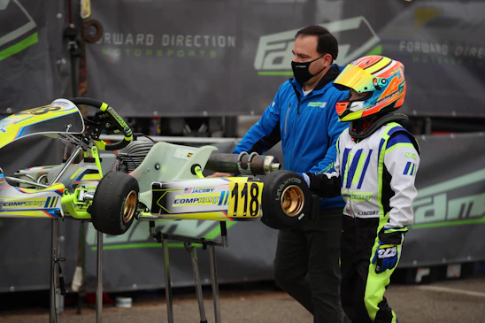 Savannah Maddox in her racing suit, helmet in hand, standing beside her kart on a sunny track.