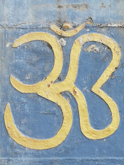 A large yellow Om symbol is painted on a weathered blue concrete wall with noticeable cracks and peeling paint.