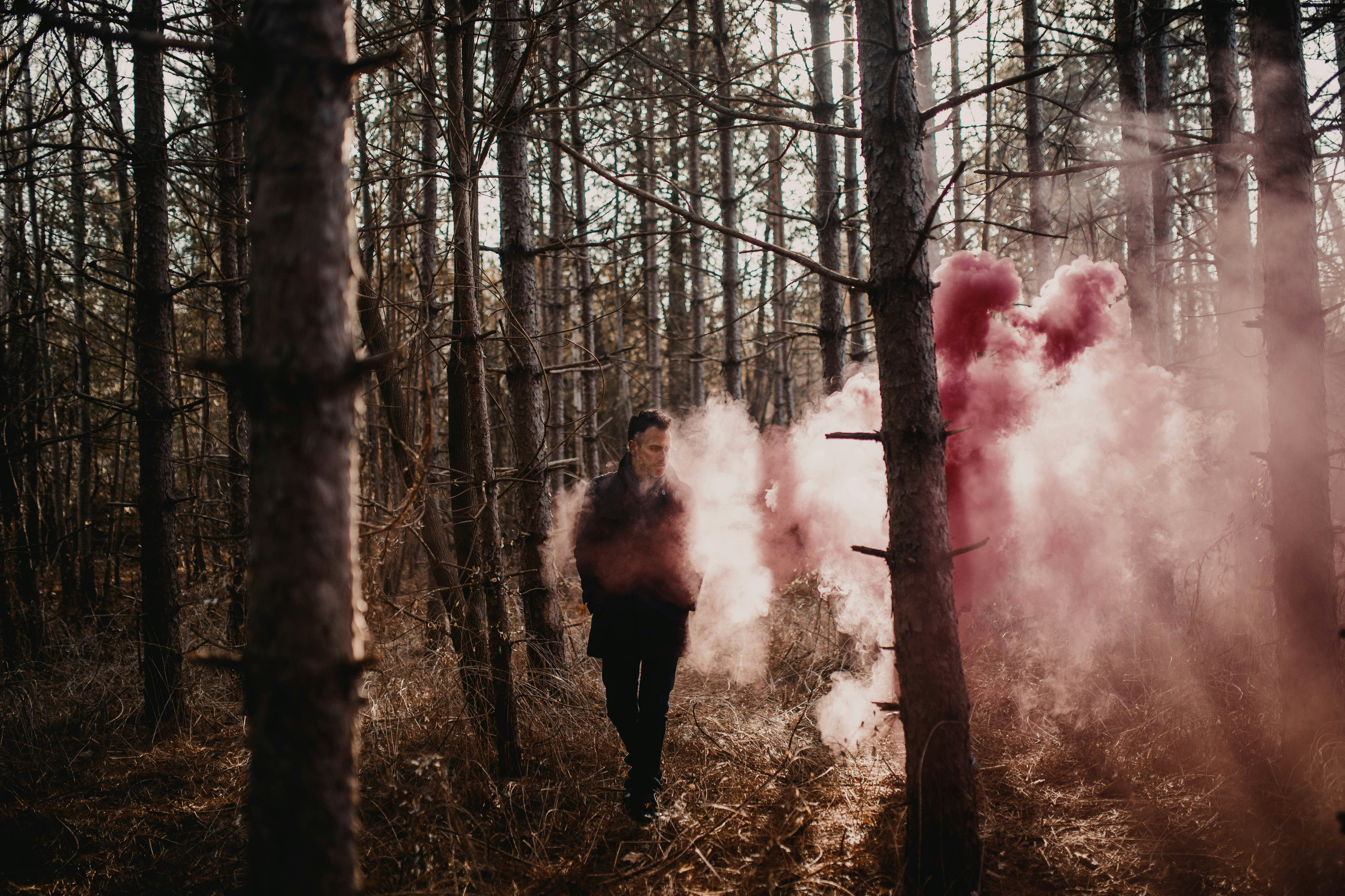Mujer en chaqueta negra de pie en el bosque con humo rojo