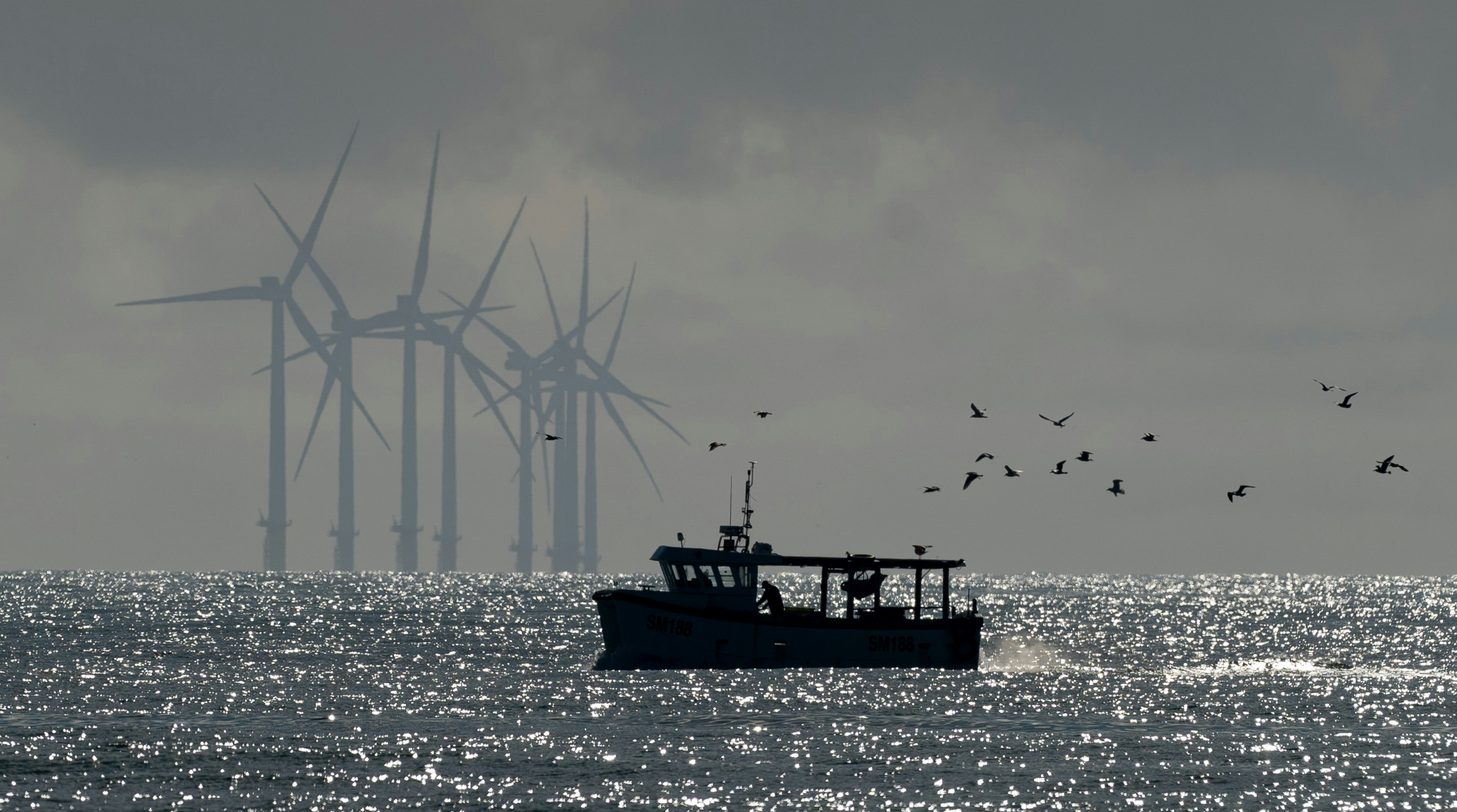 A boat in the foreground is sillouhetted against an offshore wind far in the background.