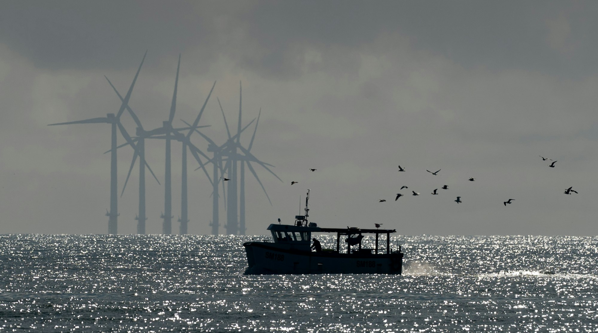 A boat in the foreground is sillouhetted against an offshore wind far in the background.