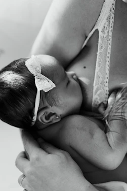 A gentle, minimalist photo of a lactation consultant guiding a mother and baby in a calm, bright room.