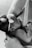 A black and white image of an infant breastfeeding. The baby is wearing a delicate headband and is held gently. The adult's arm is visible, cradling the child in a nurturing manner.