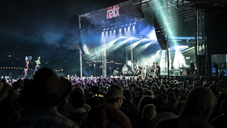 Wide shot of a large outdoor stage with colorful lights and a crowd gathering before a concert.
