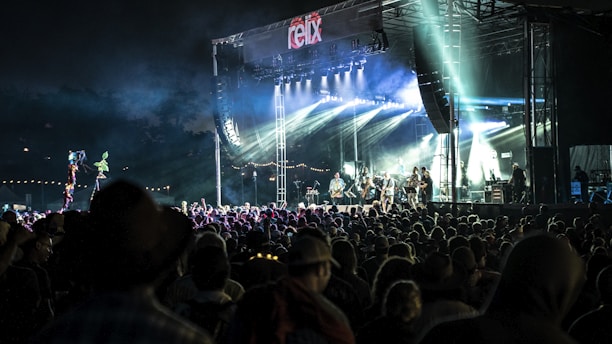 Wide shot of a large outdoor stage with colorful lights and a crowd gathering before a concert.