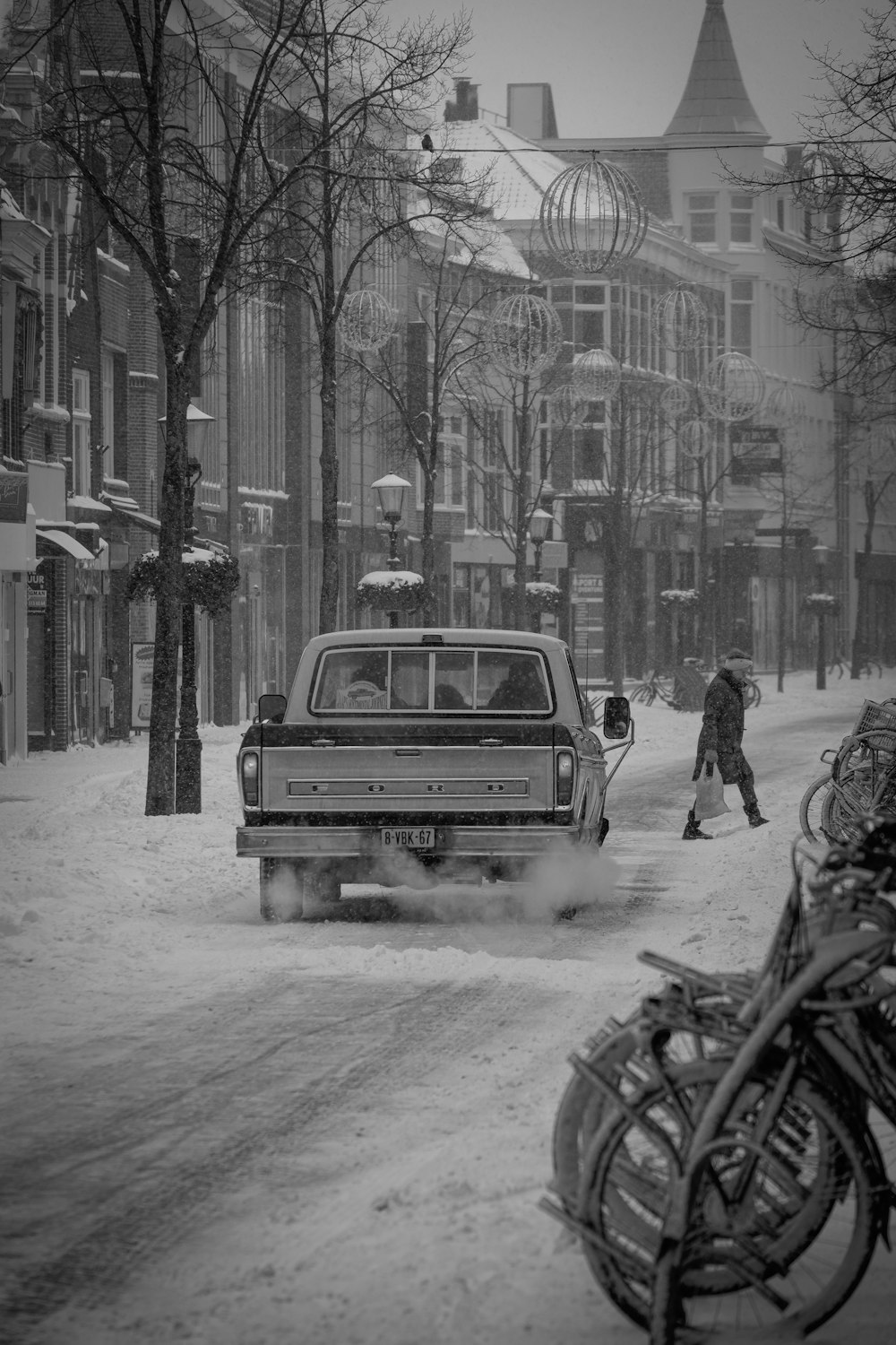 grayscale photo of man standing beside car