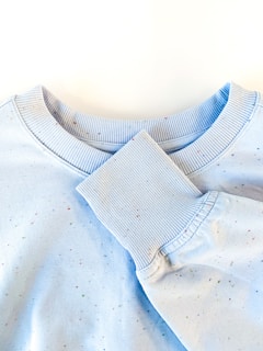 A light blue sweatshirt with ribbed collar and cuffs, adorned with small multicolored speckles.