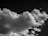 A striking black-and-white image featuring a large, fluffy cloud with various textures and shapes against a dark sky.