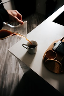 Close-up of a hand pouring fresh coffee from a ceramic pour-over into a minimalist mug.