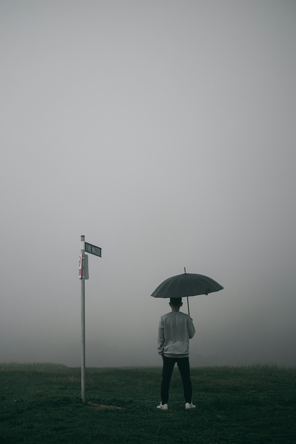 person in white jacket and gray pants holding umbrella standing on foggy field
