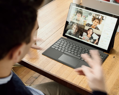 Man delivering a remote meeting with 4 other others with their cameras on and visible from within the meeting. All looking happy