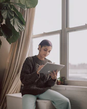 Bright and airy room with plants and a person reading a blog on a tablet.