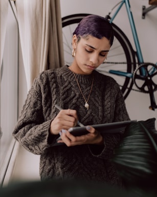 A cozy purple-hued illustration of Luna sitting by a window with plants, typing on her laptop.