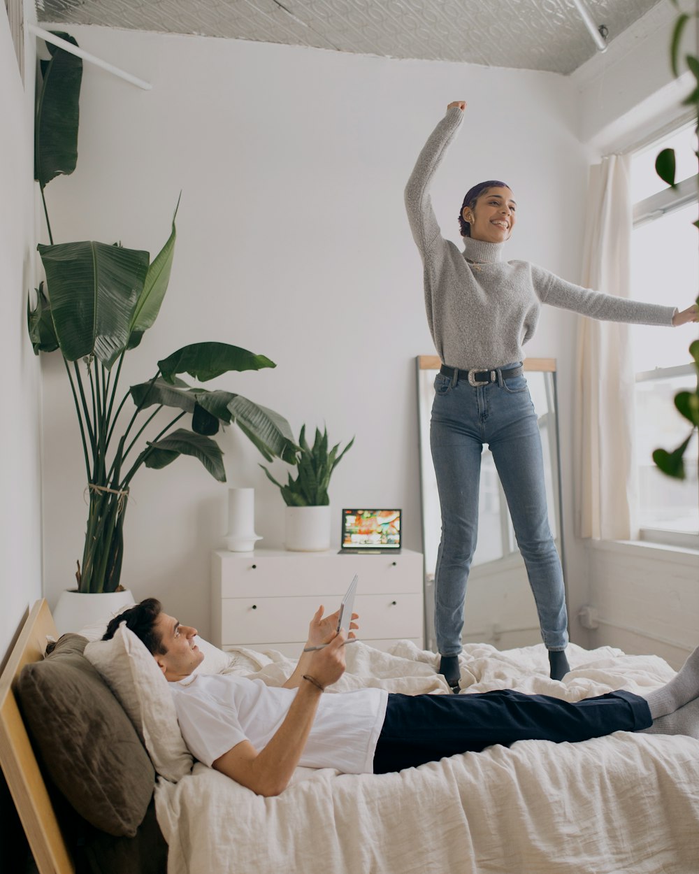 person in white long sleeve shirt and blue denim jeans standing on white bed