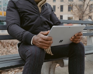 A peaceful park scene with someone using a tablet on a bench.