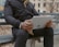 A man using a tablet outdoors with a bright city background.