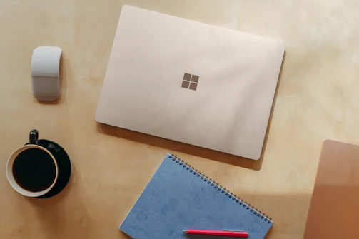 A neatly arranged workspace featuring a vintage leather-bound notebook, sapphire blue pen, and a cup of coffee on a smoky quartz taupe desk.