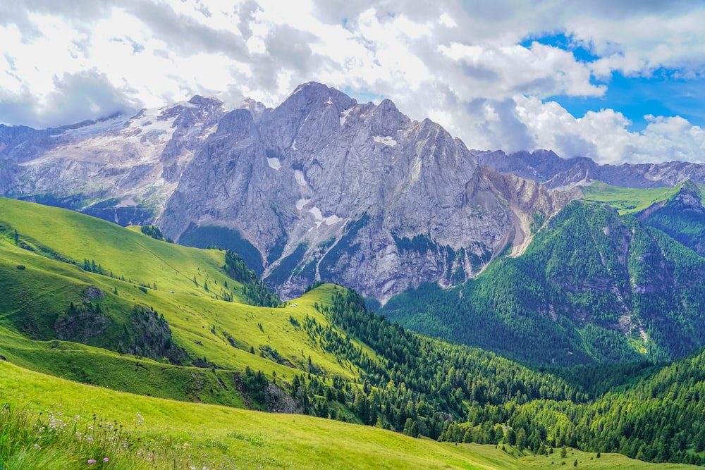 green grass field near mountain under white clouds during daytime