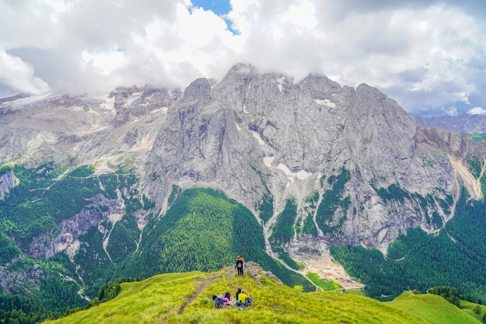 person in yellow jacket standing on green grass field near gray rocky mountain during daytime