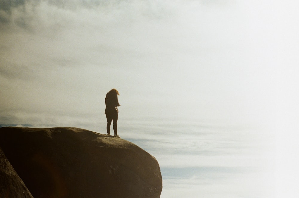 man in black jacket standing on rock formation near sea during daytime