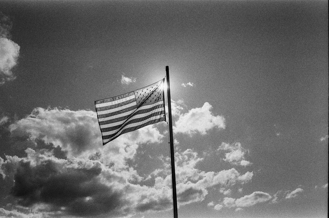 grayscale photo of us flag under cloudy sky