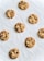 A collection of eight freshly baked cookies with chocolate chips, arranged in a random pattern on a crinkled white parchment paper. The cookies are golden brown with a soft texture and the chocolate chips are visibly embedded.