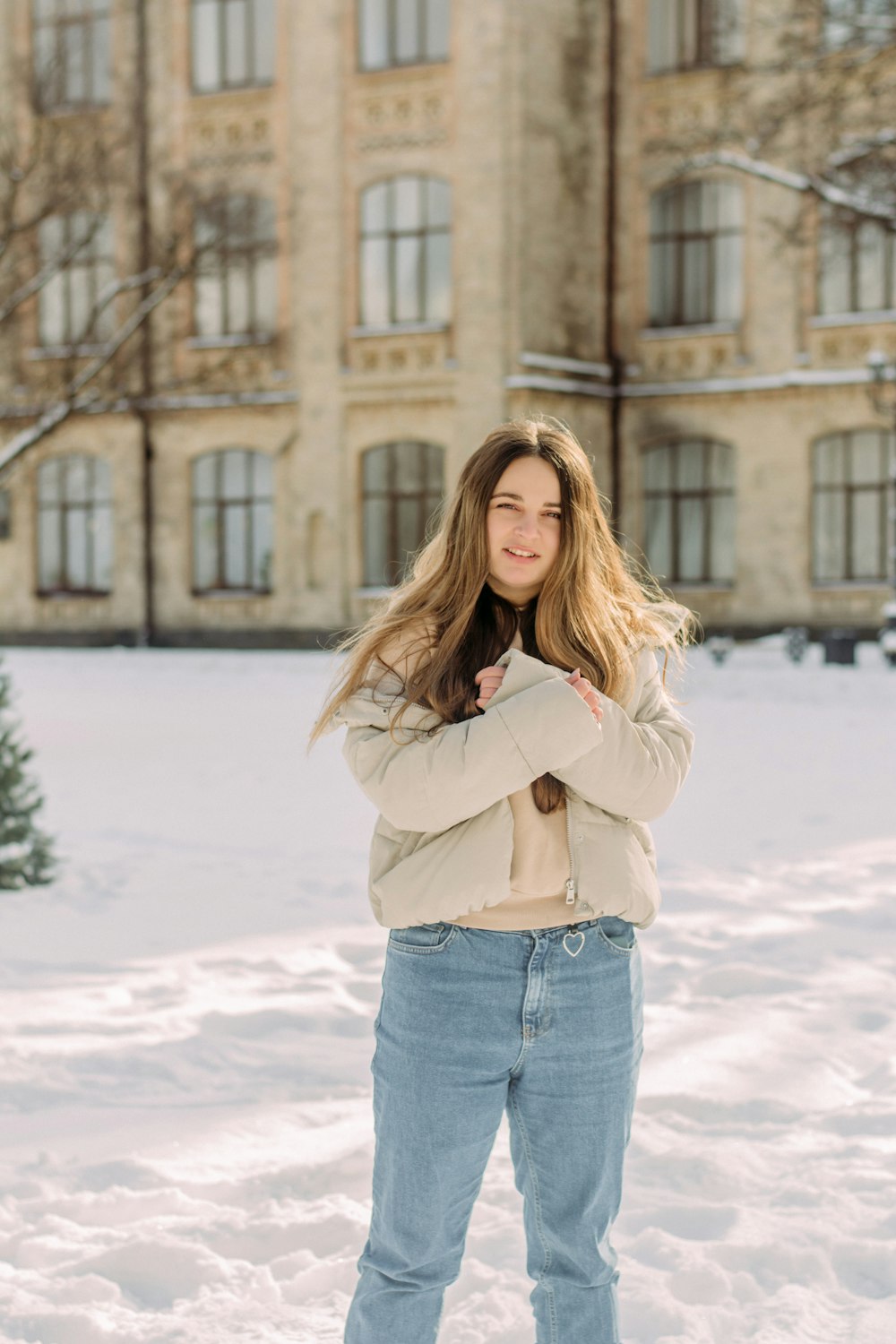 woman in beige coat and blue denim jeans standing on snow covered ground during daytime