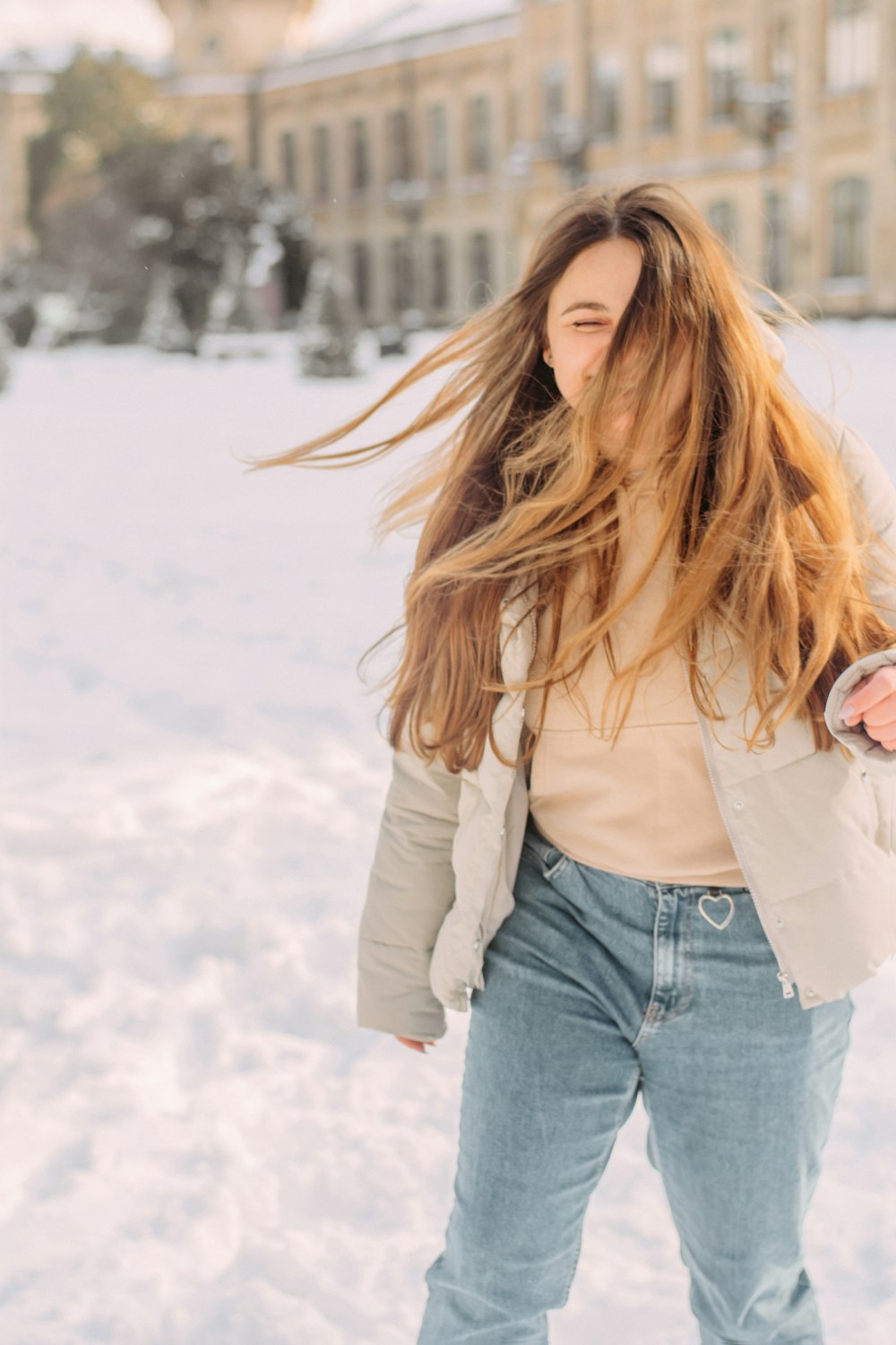 Donna in giacca bianca e jeans blu in denim in piedi su terreno coperto di neve durante il giorno