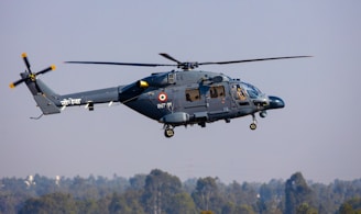 A helicopter is flying through the air with a clear view of its body and rotating blades. It has a military emblem on its side, and the pilot is visible through the windows.