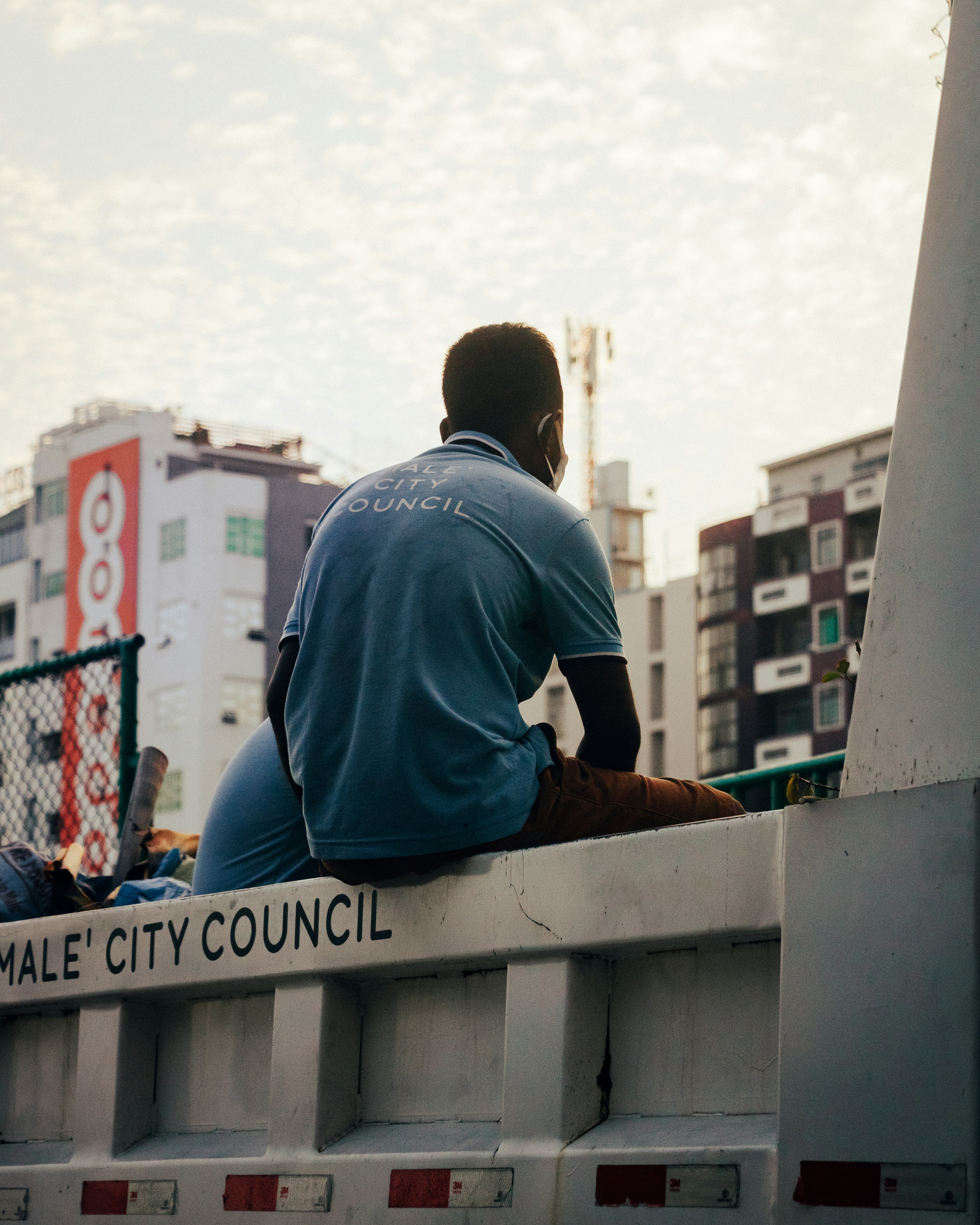 man in blue shirt sitting on brown wooden fence during daytime