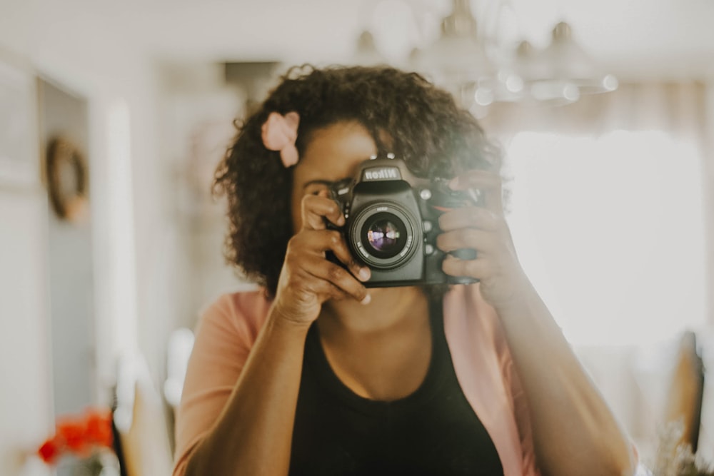 woman in black tank top holding black nikon dslr camera