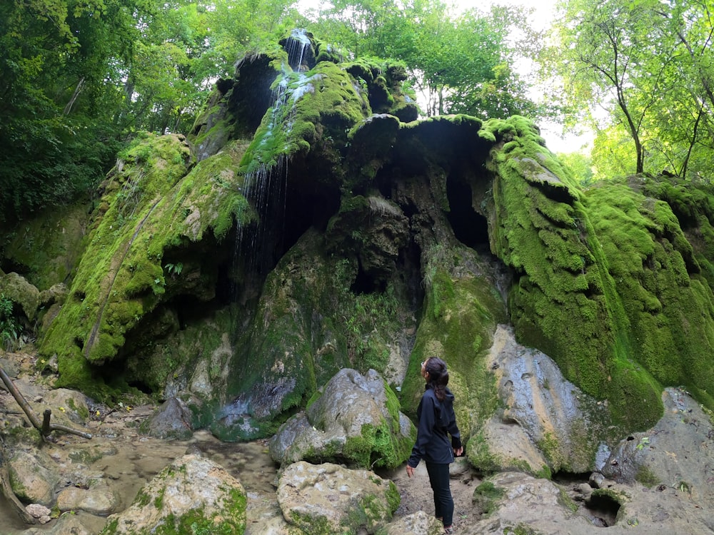 a woman standing in front of a moss covered rock formation