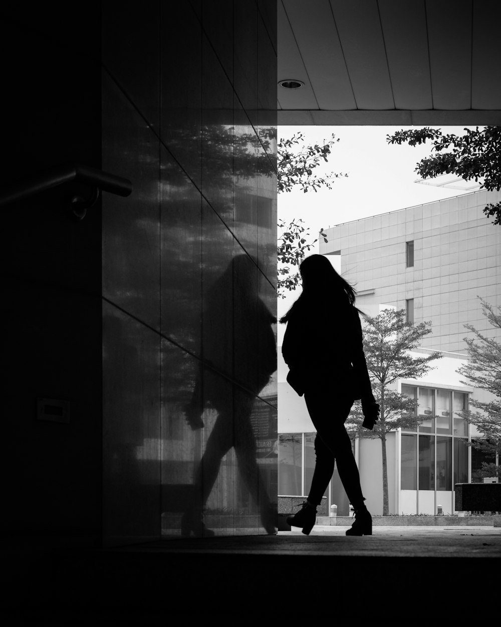 grayscale photo of man in black coat standing in front of glass wall