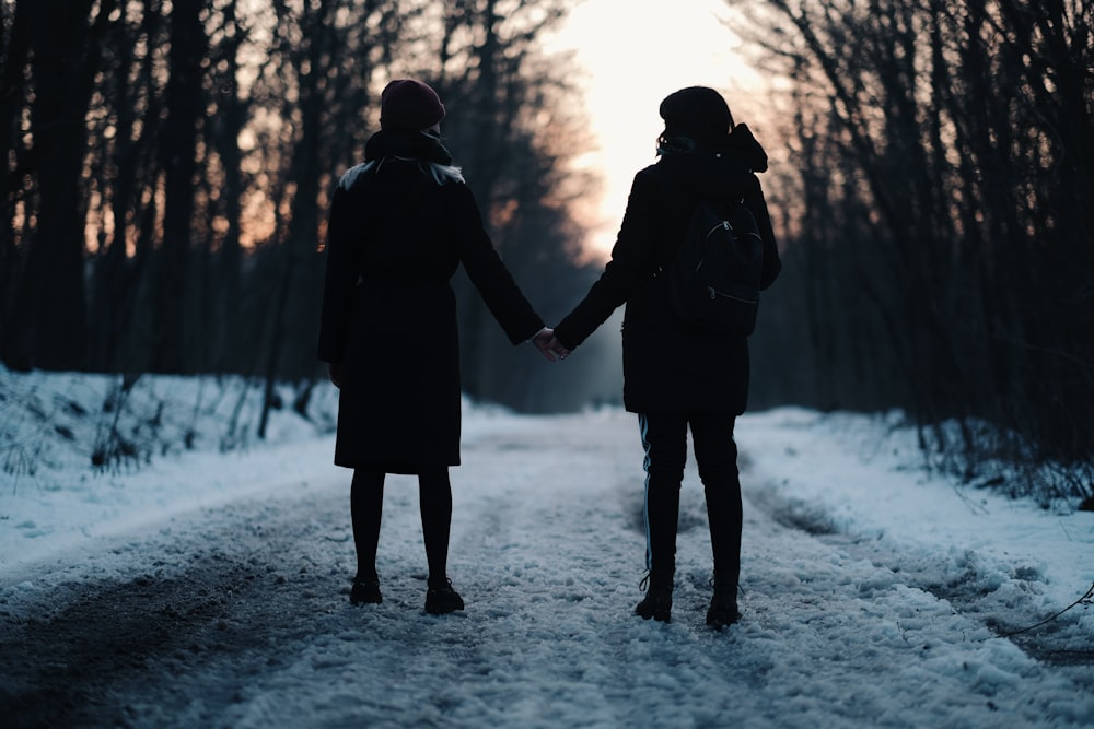 man and woman holding hands while walking on snow covered ground during daytime