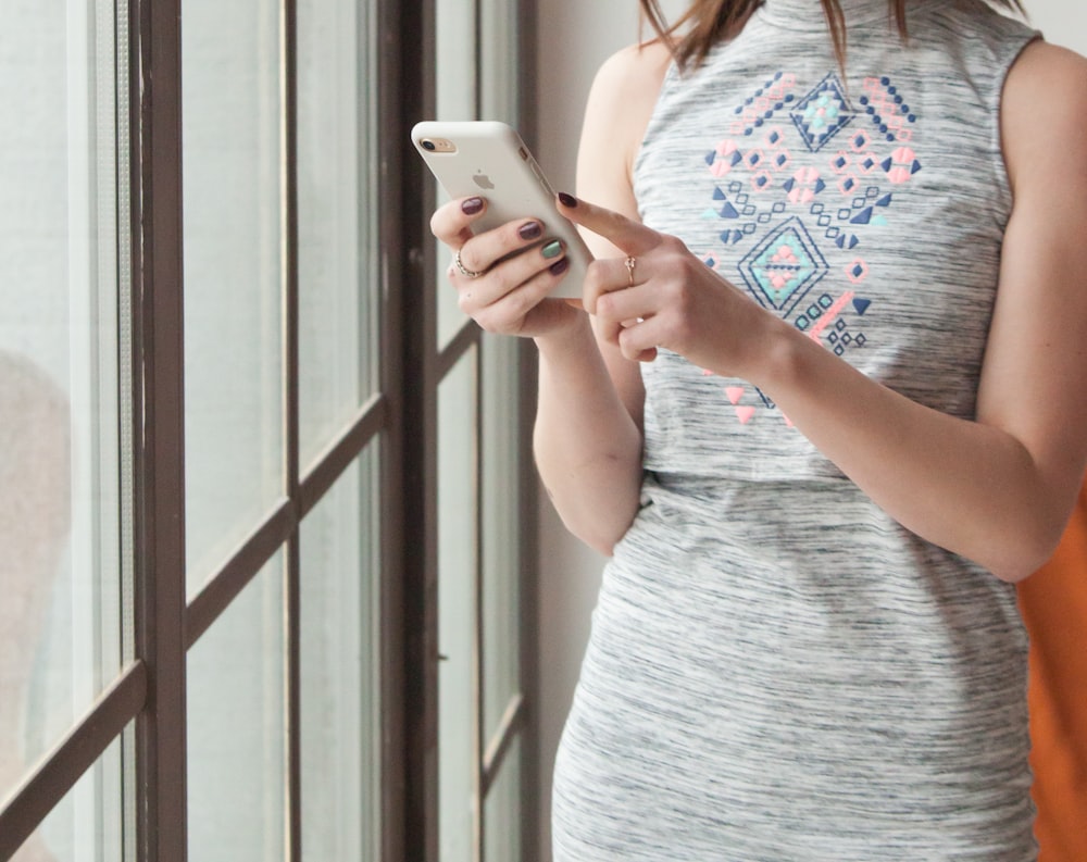 woman in gray tank top holding white smartphone