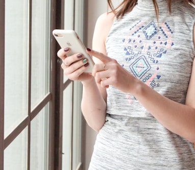 woman in gray and blue tank top holding white smartphone