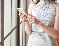 woman in gray and blue tank top holding white smartphone