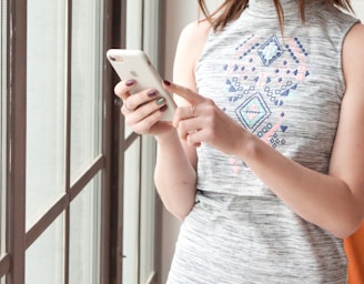 woman in gray and blue tank top holding white smartphone