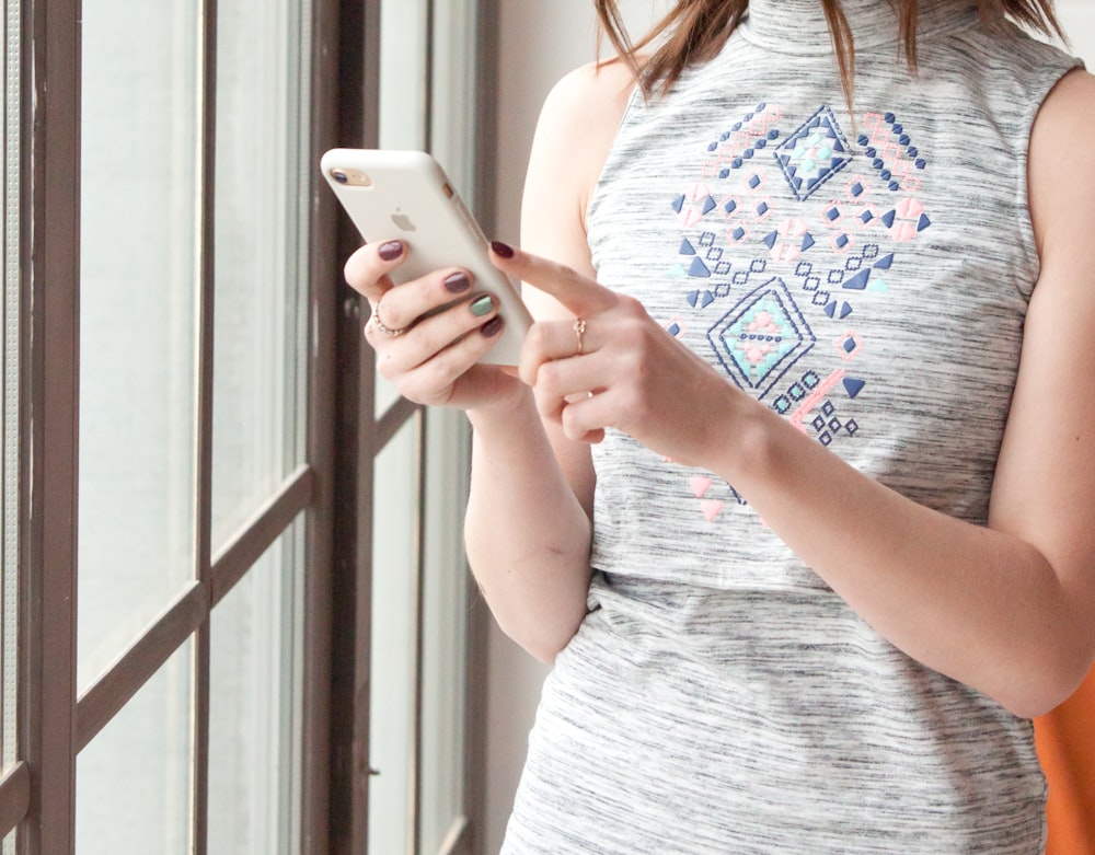 Mujer con camiseta sin mangas gris y azul sosteniendo un teléfono inteligente blanco