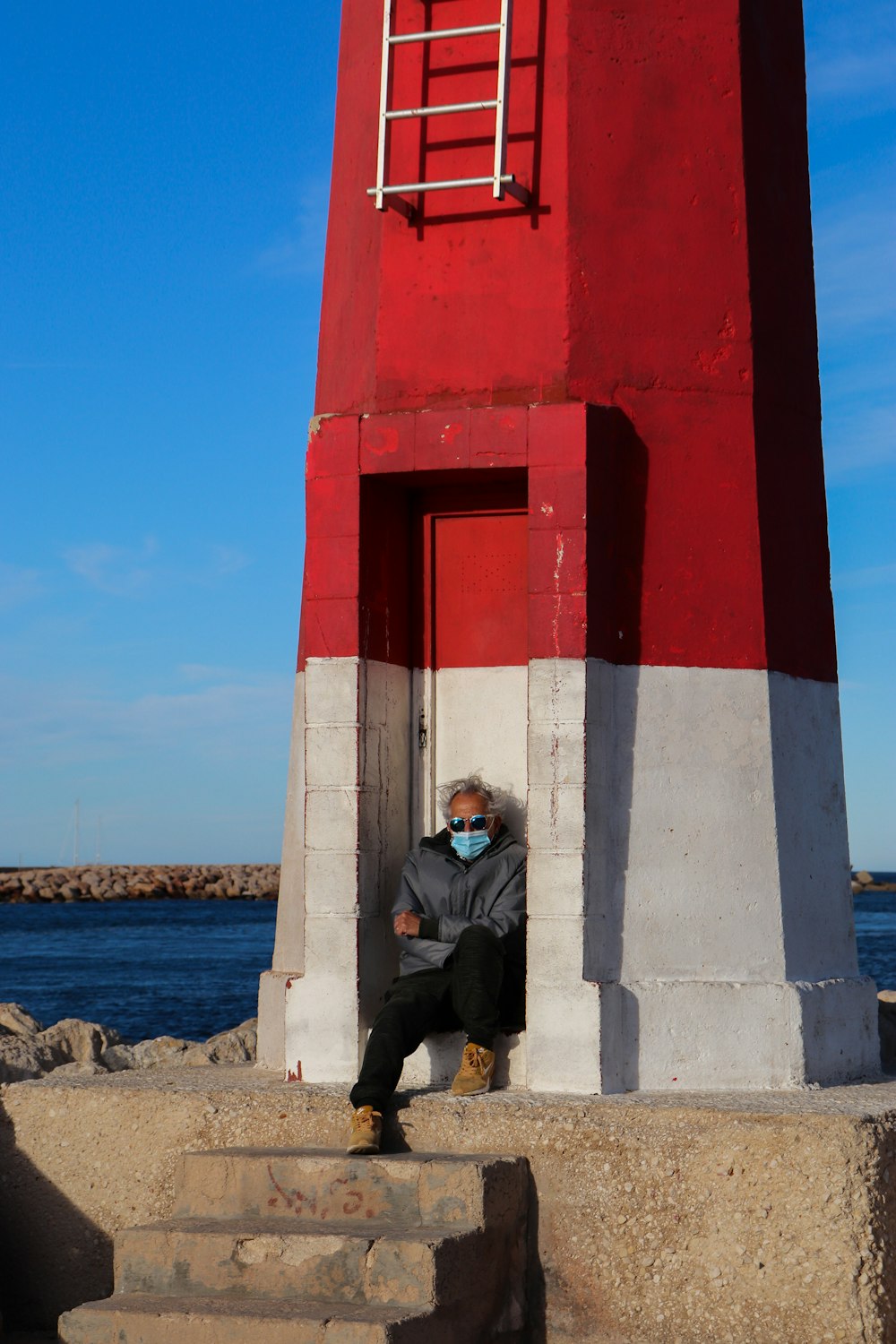 man in black jacket sitting on concrete post near body of water during daytime