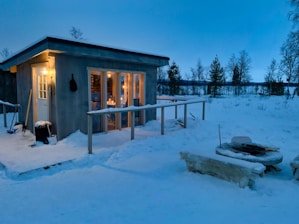Warm glow from the cabin’s fireplace visible through large windows at twilight.