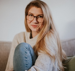 woman in blue denim jeans and white sweater sitting on gray sofa