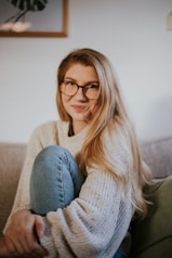 woman in blue denim jeans and white sweater sitting on gray sofa