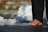 A person's bare foot is seen walking on a surface covered with patches of melting ice. The individual is wearing black pants, and the scene captures a close-up view of the foot interacting with the wet ground and crushed ice.