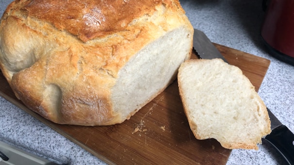 Freshly baked whole grain bread cooling on a wooden board with a knife beside it.