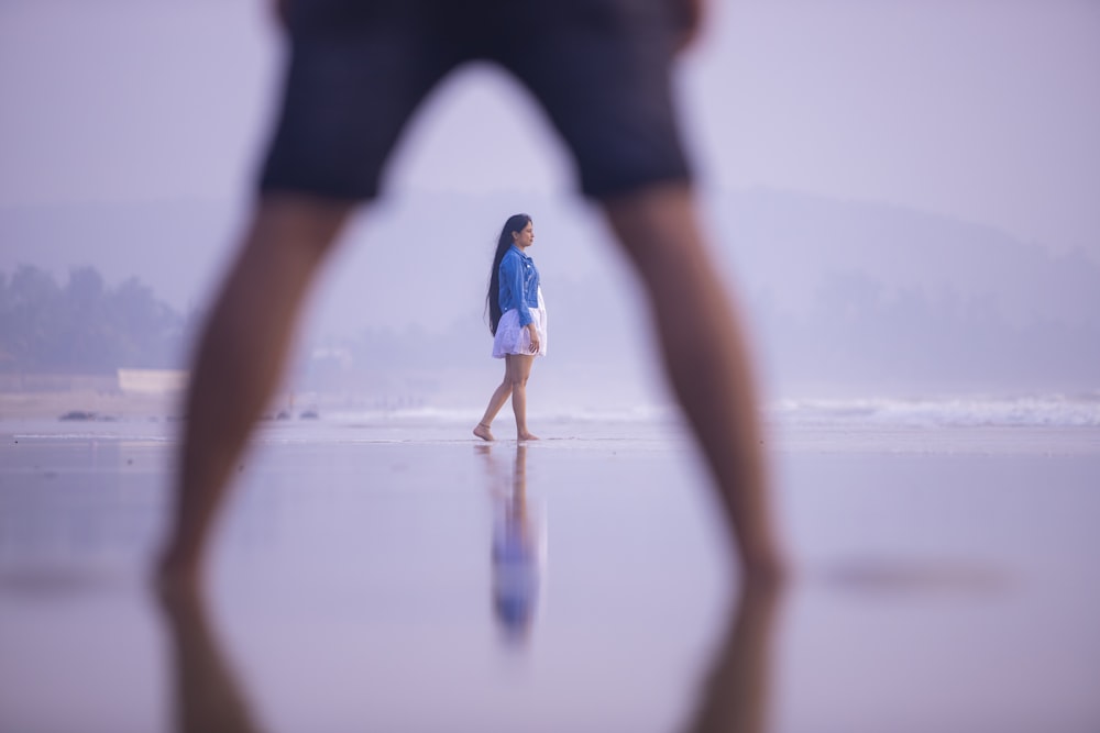 person in black pants and blue sneakers walking on the beach