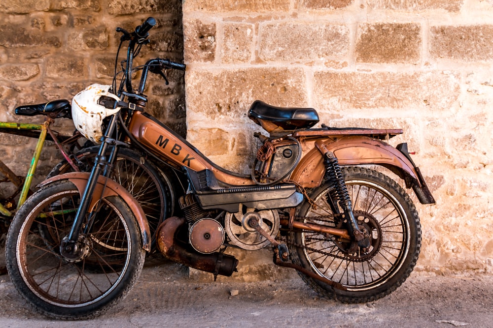 Moto standard noire et marron garée à côté d’un mur de béton blanc