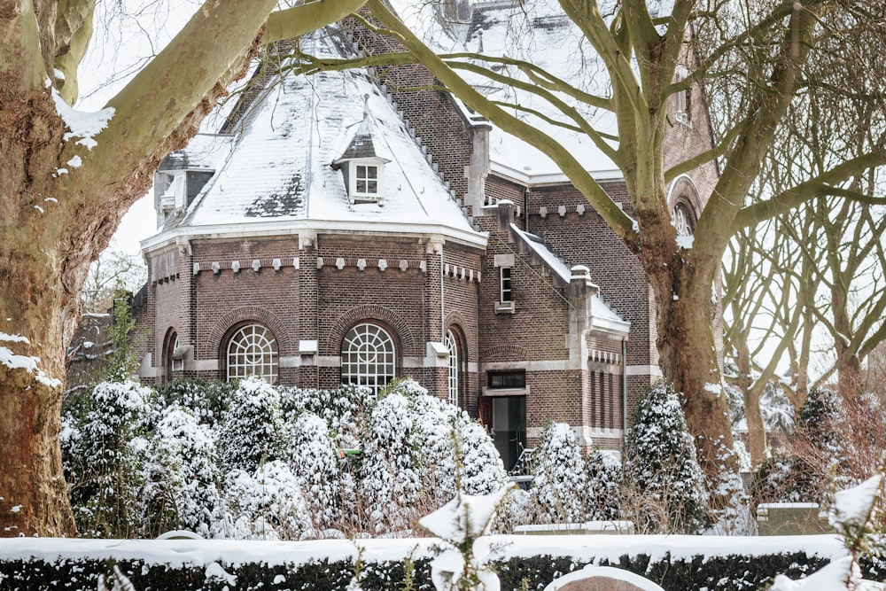 brown and white concrete house with green trees and snow covered field during daytime