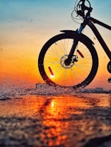 front tire and frame of black bicycle riding through shallow water during sunset