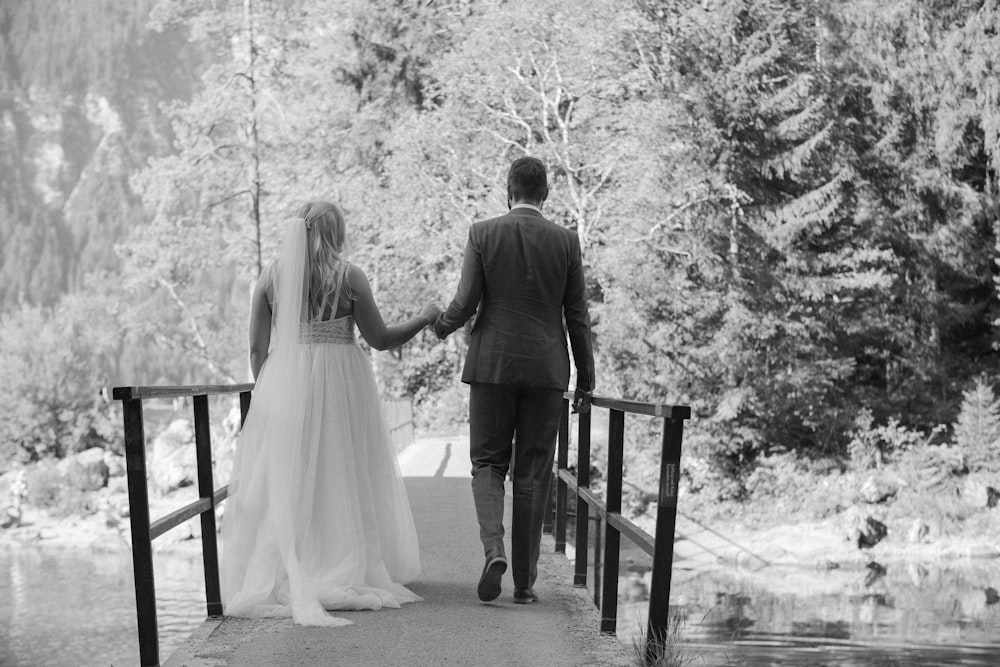 grayscale photo of man and woman standing on wooden dock